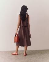 Person in a sleeveless top and flowy skirt holding a small handbag, standing indoors