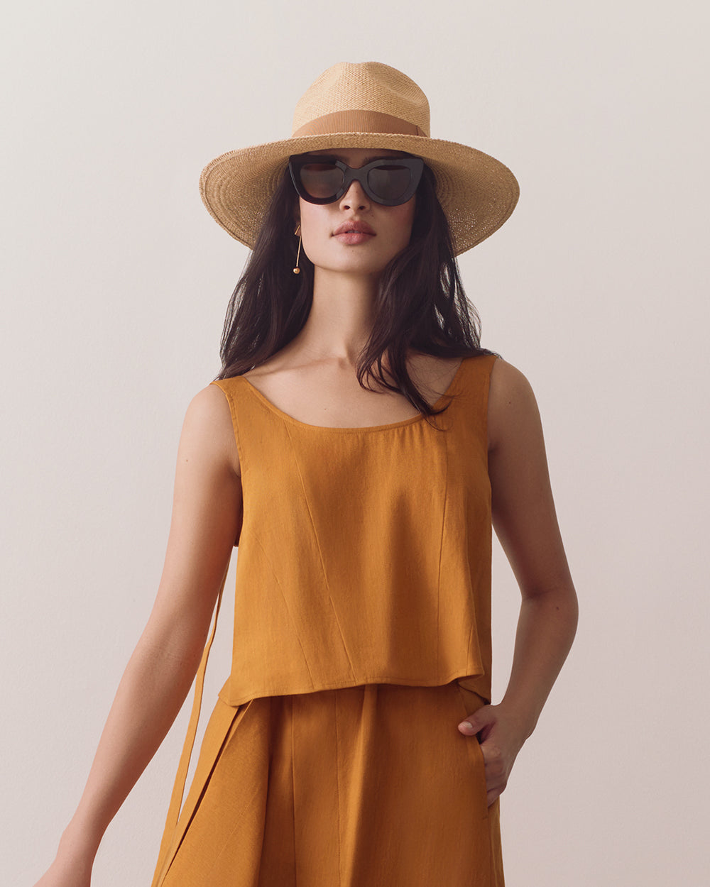 Woman in sleeveless top and pants wearing a wide-brim hat and sunglasses