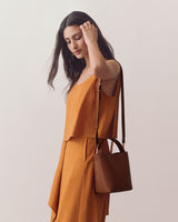 Woman in a sleeveless top and skirt holding a shoulder bag.