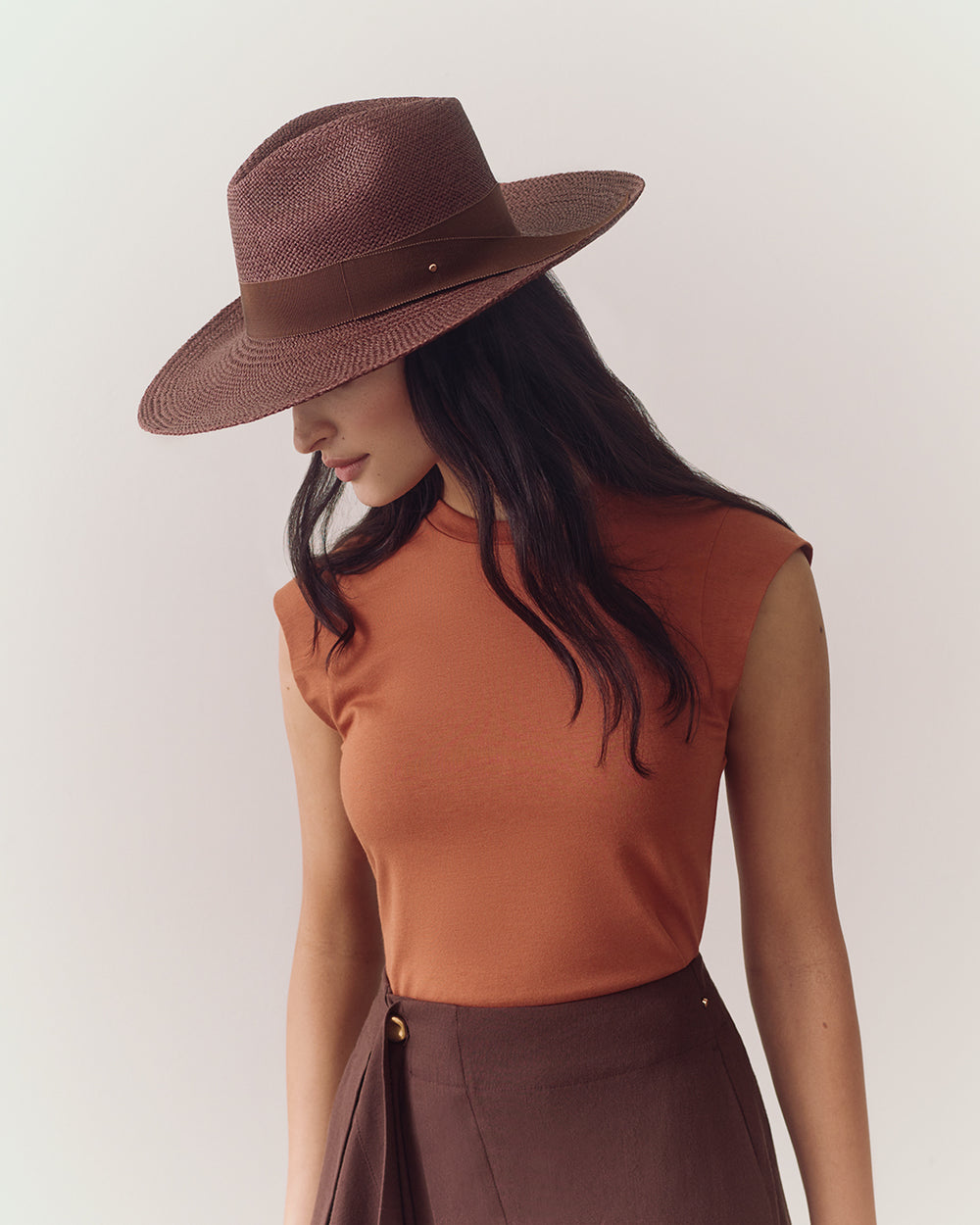 Person wearing sleeveless top, wide hat, and a skirt with side button.