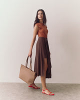 Woman holding a large tote bag wearing a sleeveless top and a flowy skirt with sandals.