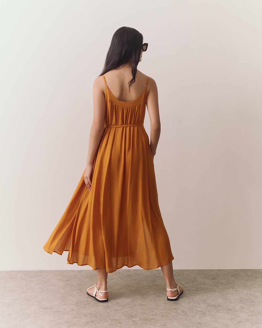 Woman in long dress facing away, wearing sandals and sunglasses