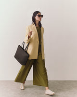 Person wearing blazer and pants, holding a tote bag, and walking.