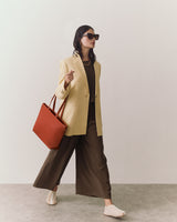 Person in a blazer and wide pants carrying a tote, wearing sunglasses.