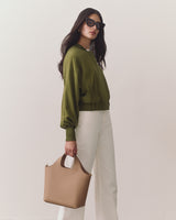 Woman in jacket and pants holding a tote bag, wearing sunglasses, facing left