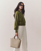 Person wearing sunglasses, holding a handbag, dressed in a jacket and pants.