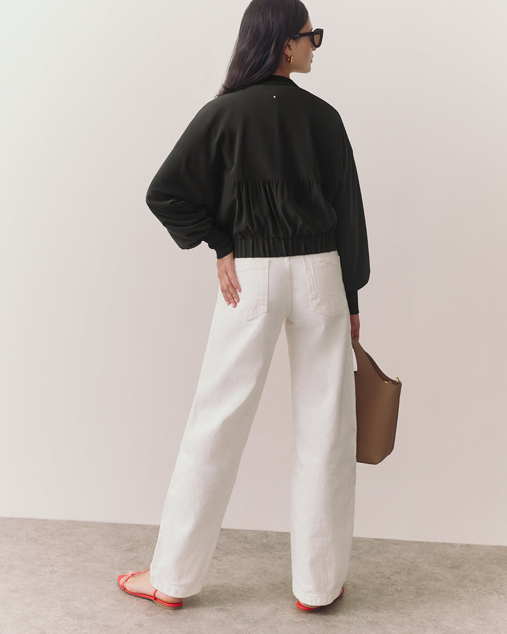 Woman wearing jacket and pants holding a handbag, facing away.