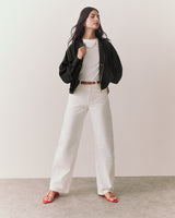 Person wearing a jacket, shirt, pants, and sandals, standing on a plain floor.