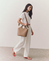 Person walking with a handbag wearing a white outfit with red sandals.