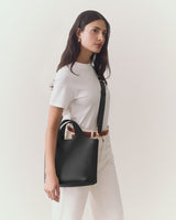 Person holding a handbag stands against a plain background.