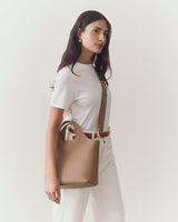 Person standing with a handbag, wearing a shirt and pants.