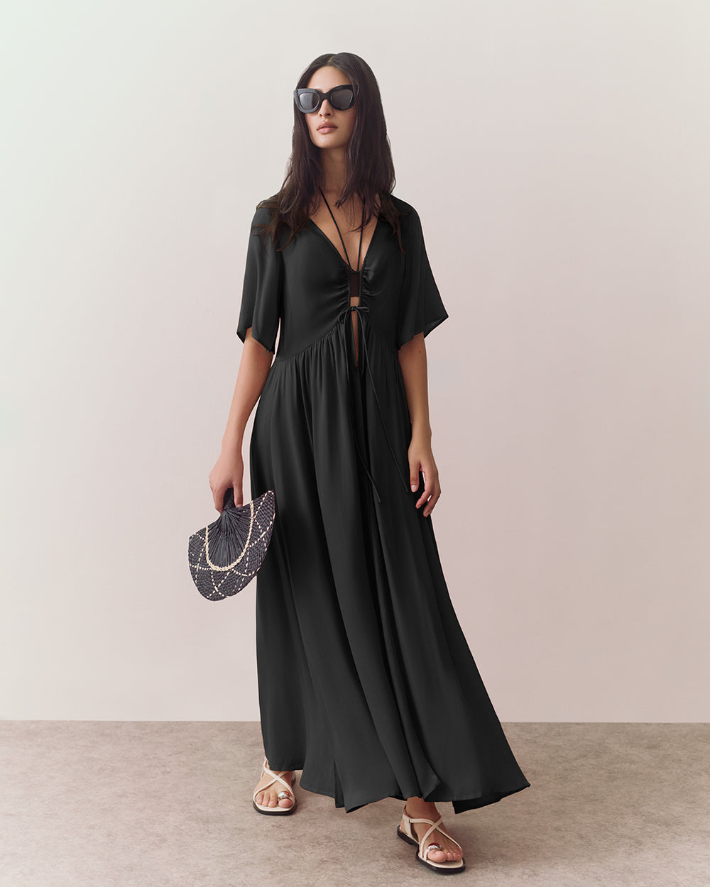 Woman in a long dress with sunglasses holds a fan.