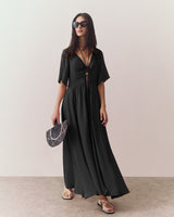 Woman in a long dress with sunglasses holds a fan.