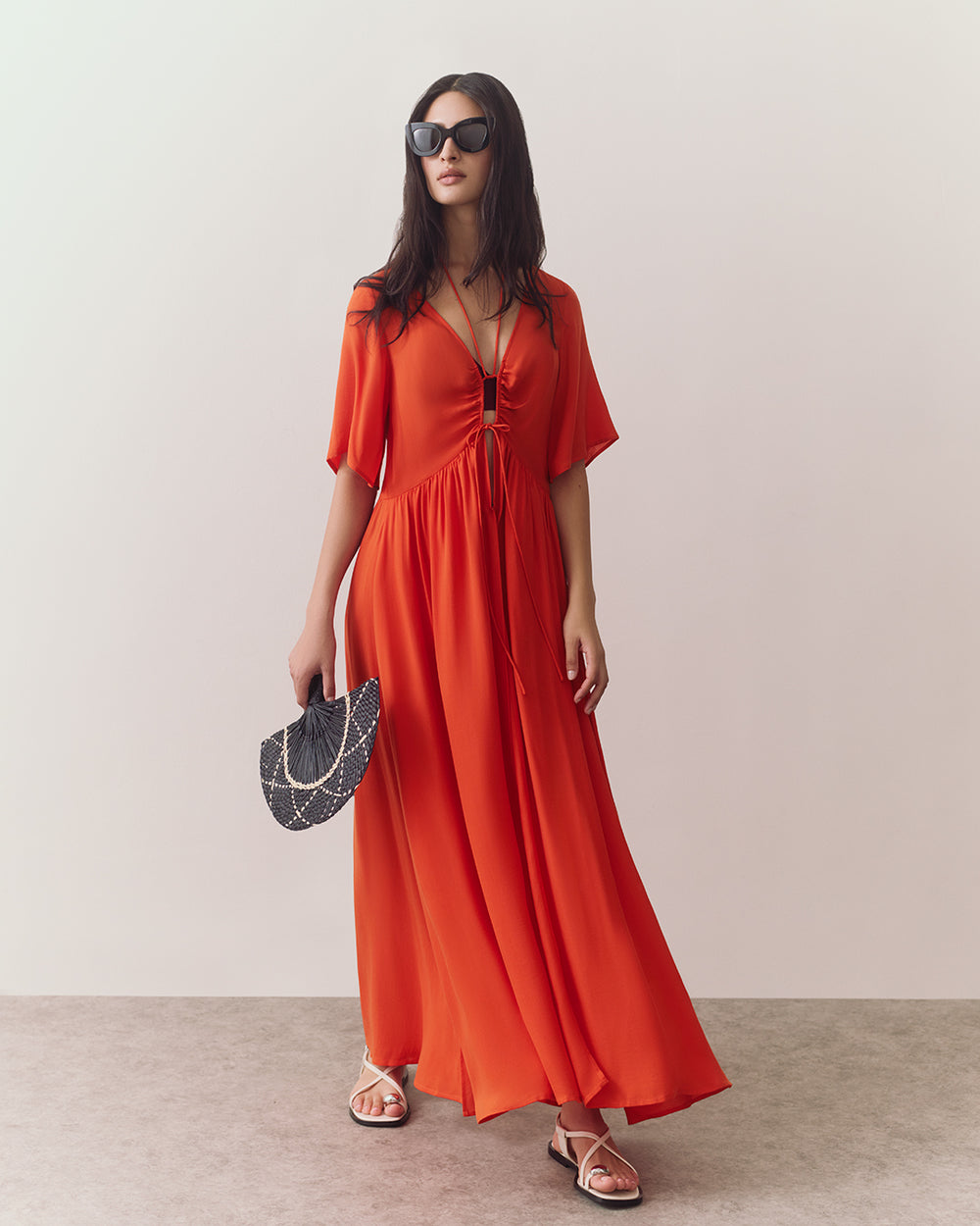 Woman in flowing dress, sunglasses, holding a bag, wearing sandals.