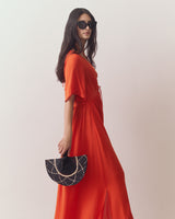 Woman in long dress holding a woven fan wearing sunglasses.