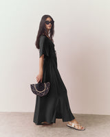 Person wearing long dress and sunglasses holds a fan standing indoors