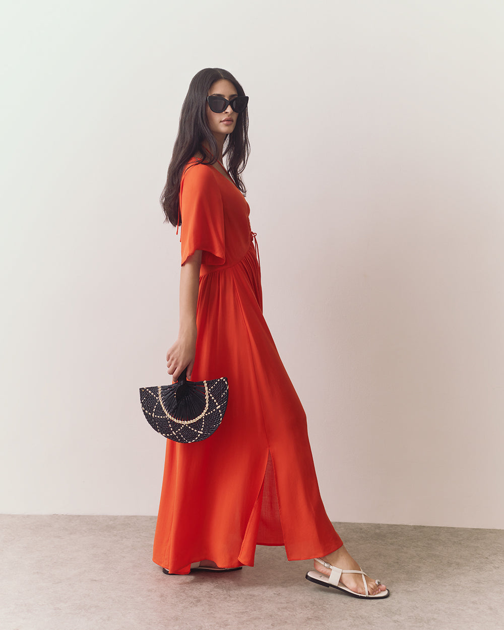 Person in a swimsuit coverup with sunglasses holds a fan and walks forward.