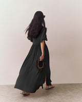 Person wearing long dress and sandals, holding a fan, walking away.