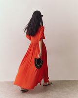 Person in flowing swimsuit coverup holding a fan walking away on flat surface