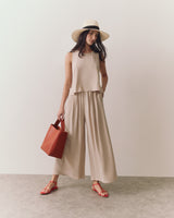 Woman in wide-leg pants, sleeveless top, sun hat, holding a tote, wearing strappy sandals.