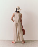 Woman in wide-leg pants with a sleeveless top, wearing a hat, holding a bag.