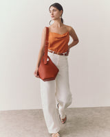 Woman in a tank top and pants, holding a shoulder bag.