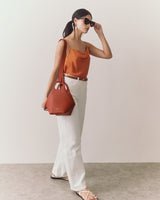 Woman wearing a tank top with thin straps and jeans holding a handbag.