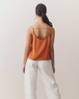 Woman wearing a tank top with thin straps and jeans holding a handbag.
