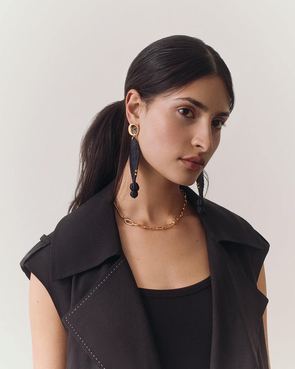 Palma Drop Earrings Person wearing a vest, earrings, and necklace, looking off to the side.