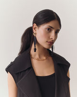 Person wearing a vest, earrings, and necklace, looking off to the side.