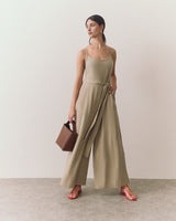 Person wearing jumpsuit with belt holds handbag and stands on a plain background.