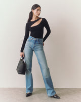 Person in a cutout top and jeans holding a handbag.
