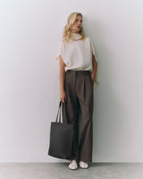 Person in a top and pants standing with a tote bag and looking left