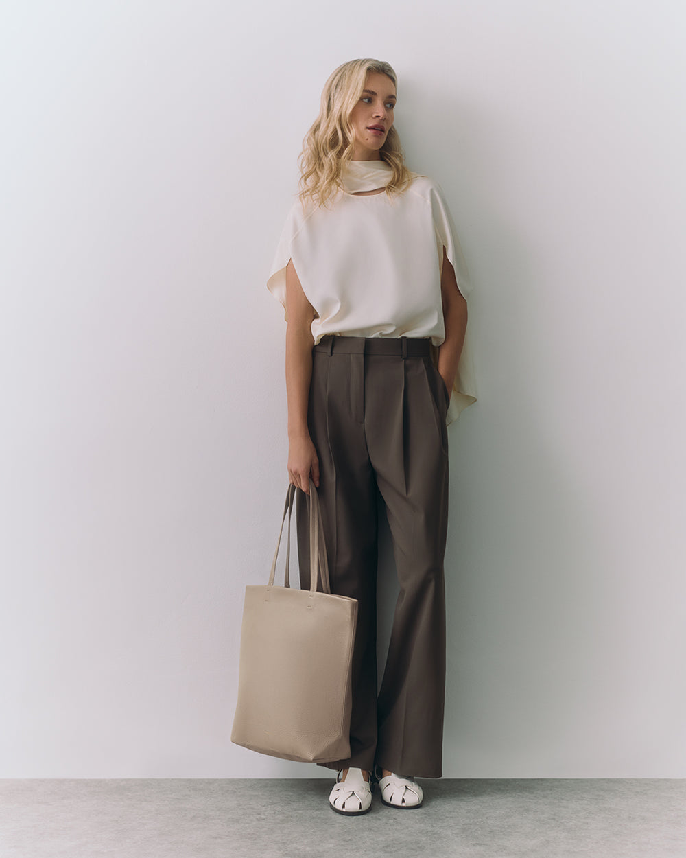 Tall Easy Tote Person standing against wall wearing top and pants holding a tote bag in one hand.