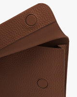 Close-up of a textured leather bag flap with button closure.
