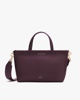 A handbag with a top handle, detachable shoulder strap, and small gold embossed text.