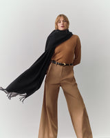 Person wearing a long-sleeve top, wide-leg pants, and a scarf draped over one shoulder.