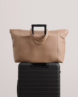 Travel bag with a luggage sleeve placed on top of a suitcase with extended handle