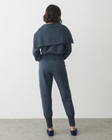 Person in matching outfit with cape, facing away, standing in a neutral space.