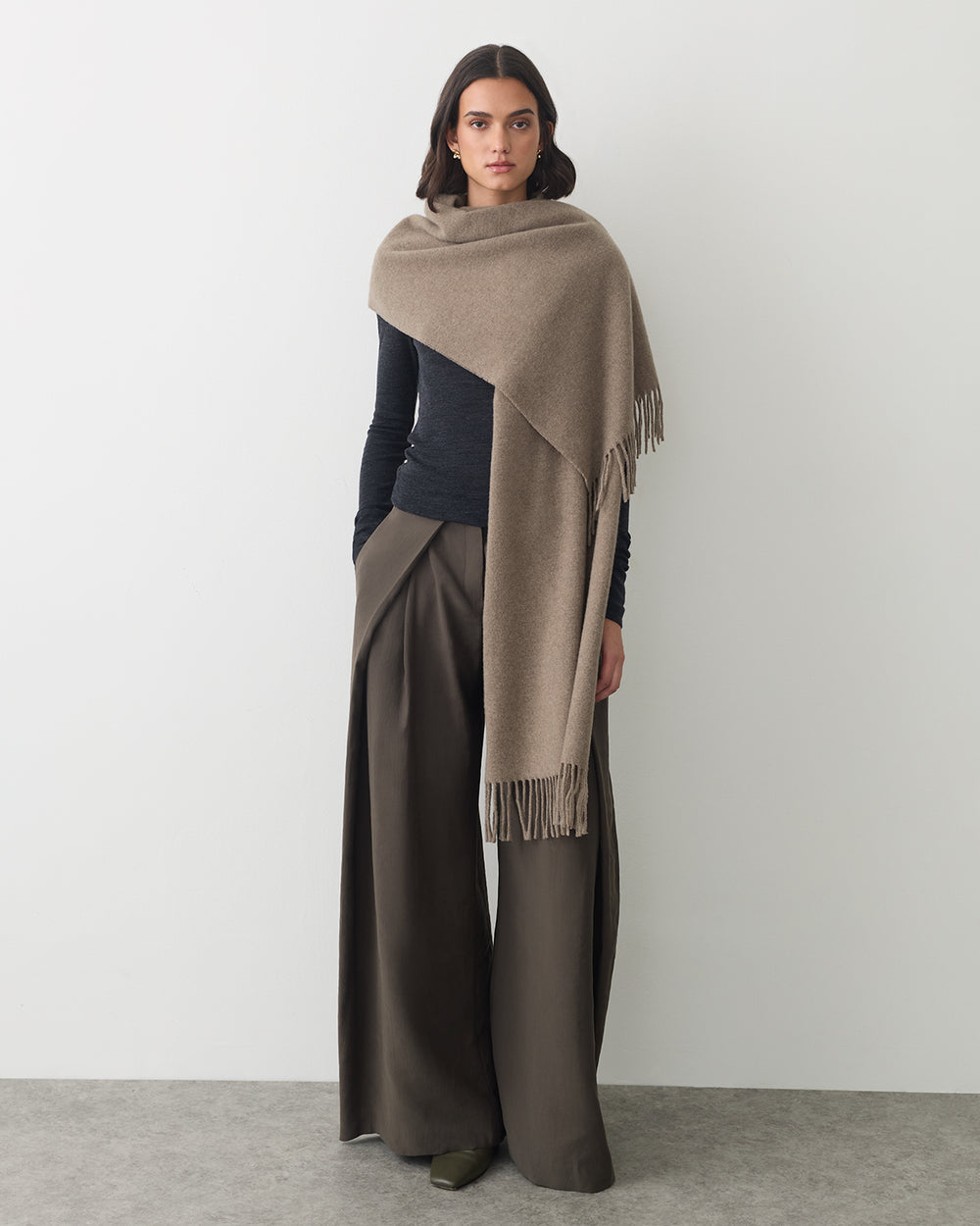 Person wearing a cape, long-sleeve top, and wide-leg pants standing against a plain backdrop.