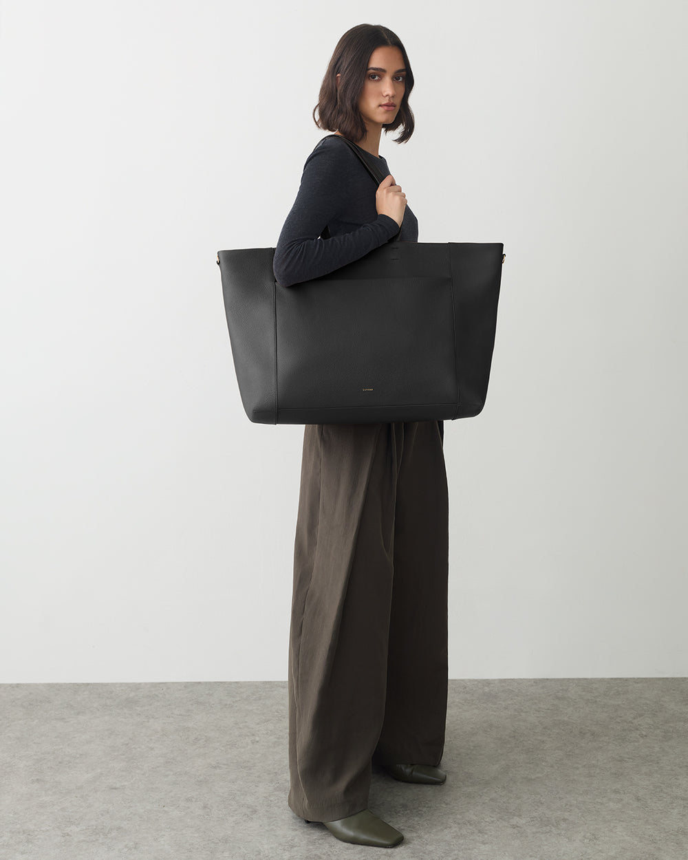 Person standing with a large tote bag, wearing wide-legged pants and holding bag on shoulder.