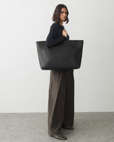 Person standing with a large tote bag, wearing wide-legged pants and holding bag on shoulder.
