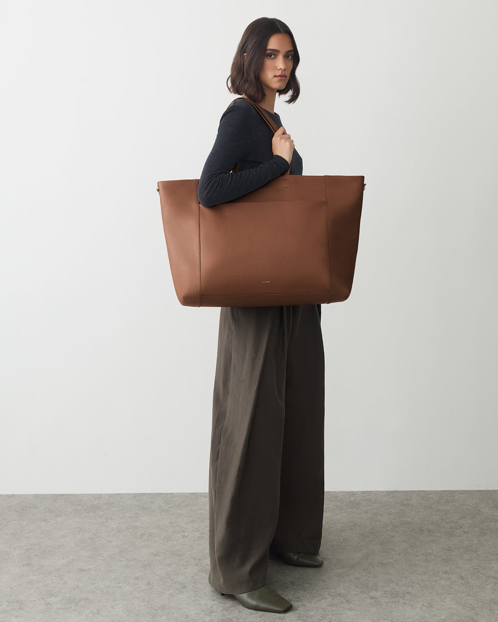 Person carrying a large tote bag, wearing wide-leg pants and a long-sleeve top.