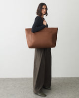 Person carrying a large tote bag, wearing wide-leg pants and a long-sleeve top.