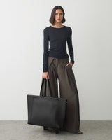 Person with long-sleeve shirt, wide pants, holding large bag standing indoors