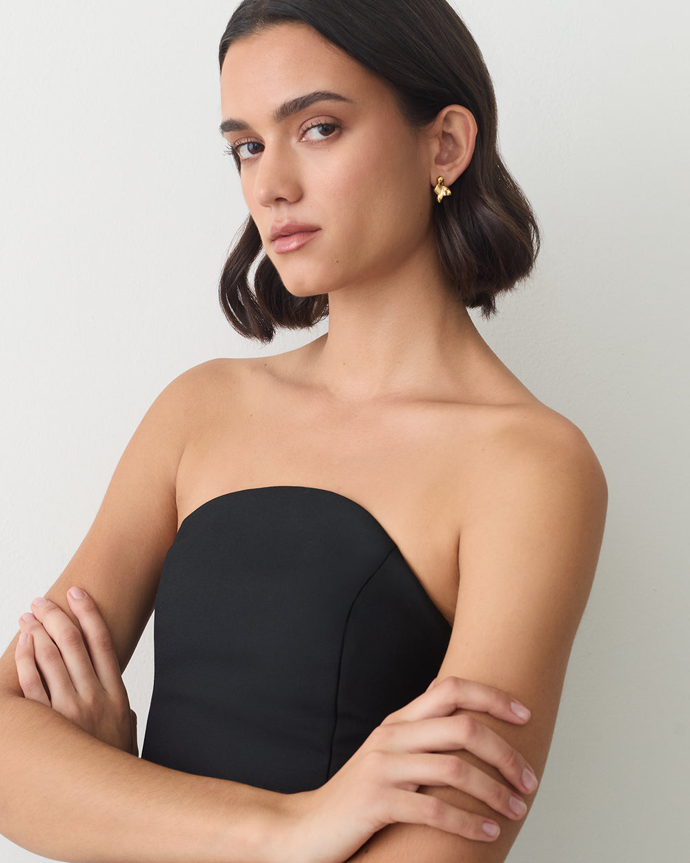 Person wearing a strapless top and earrings, arms crossed, looking at the camera.