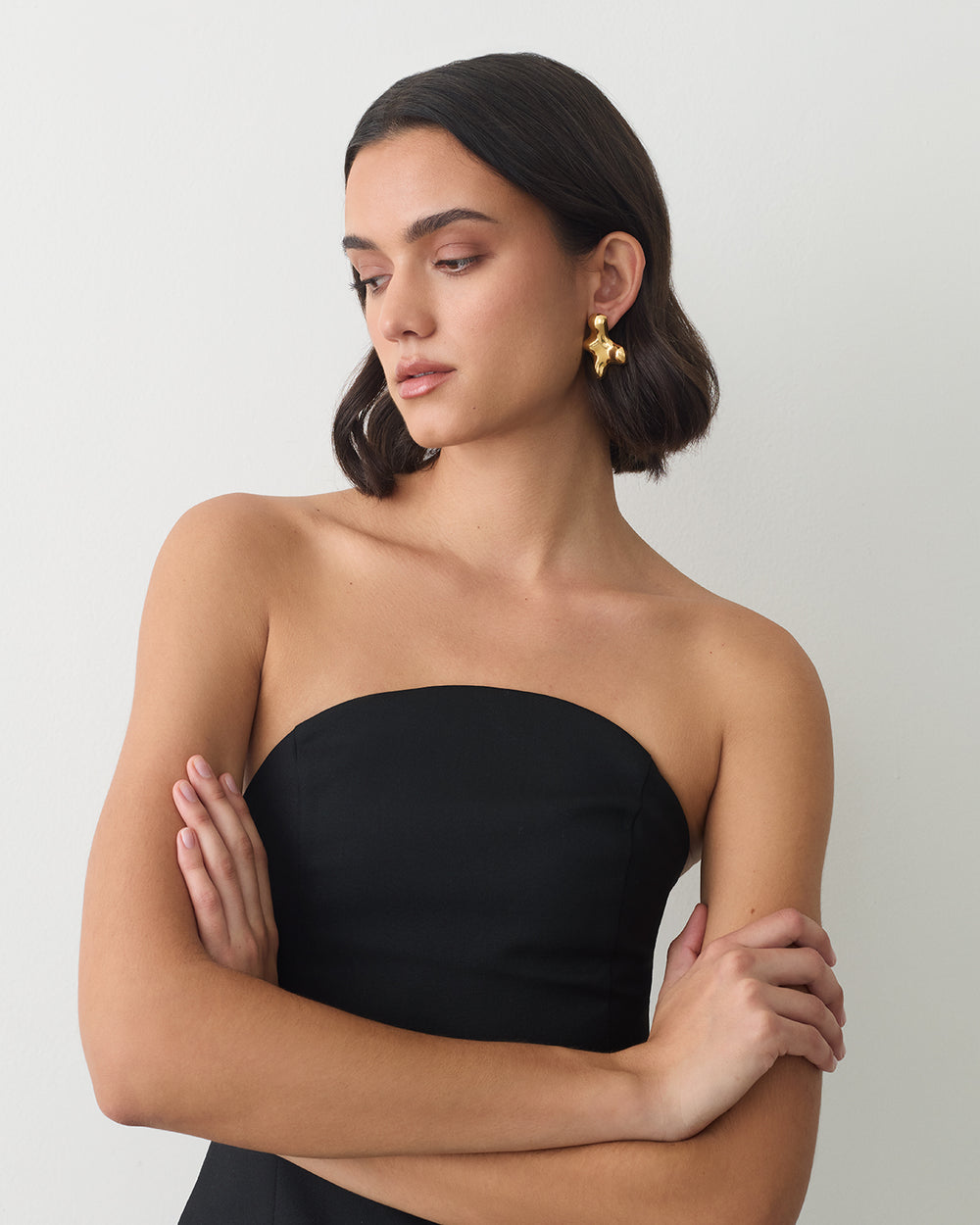 Person wearing a strapless top and earrings, arms crossed, looking to the side.