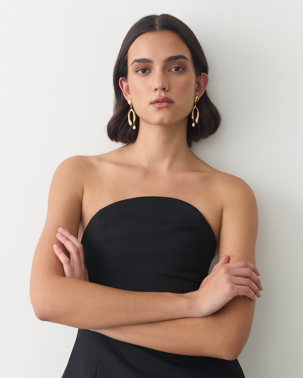 Person wearing strapless top with arms crossed, gold hoop earrings.