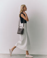 Person walking with a shoulder bag, wearing a sleeveless top and long skirt.