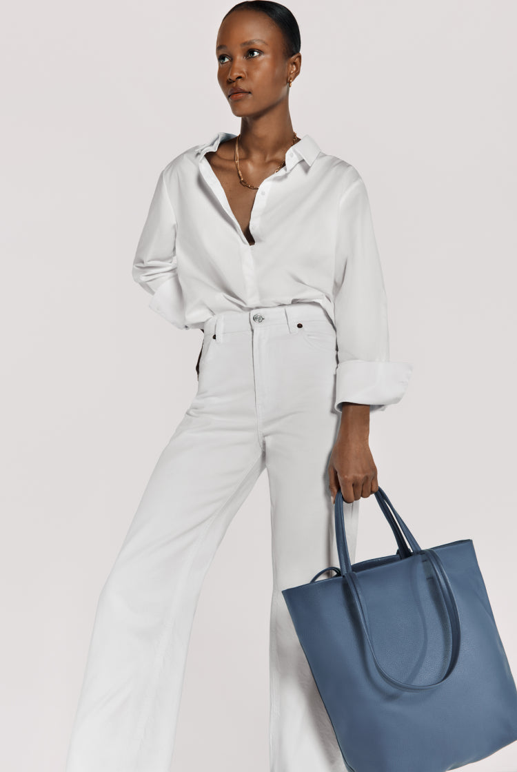 Woman standing with handbag, wearing an outfit with a collar and belt.